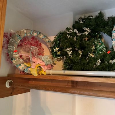 Assorted seasonal wreaths, including a spring-themed fabric wreath and a green faux-evergreen holiday wreath, stored on a closet shelf.