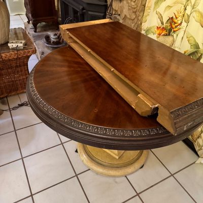 Round wooden pedestal dining table with a sunburst veneer top, carved egg-and-dart border, and an accompanying table leaf.