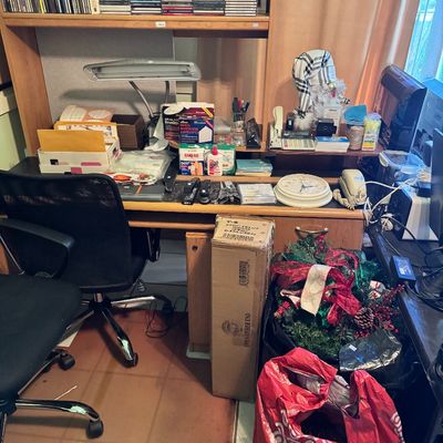 Wooden home office desk with hutch, featuring a black mesh office chair, desk lamp, and various office supplies, CDs, and holiday...