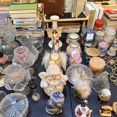 Assortment of holiday decor, glassware, and candles, including a ceramic snowman figurine, cut-glass pitchers, and jar candles, displayed...