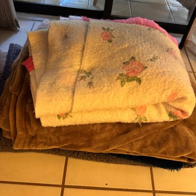 Stack of vintage blankets, including a cream-colored thermal blanket with a pink rose pattern and a solid brown plush blanket.