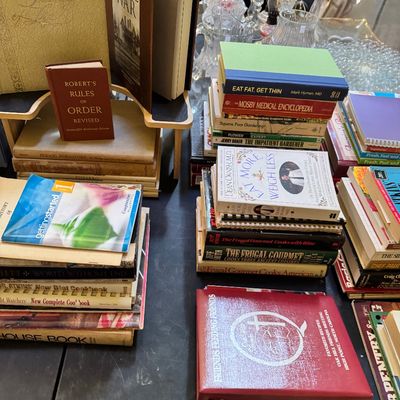 Assorted vintage and modern books, including cookbooks, medical guides, and historical texts, displayed on a black folding table.