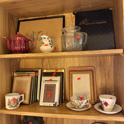 Assorted vintage collectibles displayed on wooden shelves, including a maroon ceramic teapot, a clear glass pitcher, various picture...