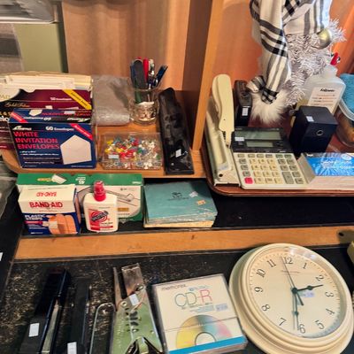 Assorted office supplies and desk accessories, including staplers, a calculator, a wall clock, envelopes, and a CD-R, arranged on a...