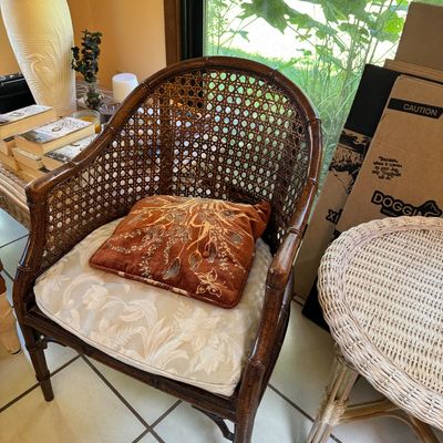 Vintage faux-bamboo armchair with a woven cane back, featuring a cream floral seat cushion and an embroidered rust-colored accent pillow.