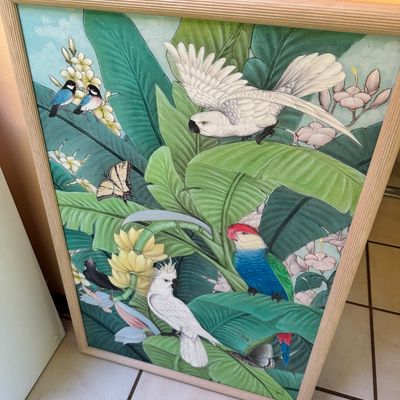 Large framed tropical art print featuring cockatoos, parrots, and butterflies amidst lush green foliage, housed in a light wood frame.