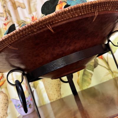 Decorative hammered bowl with a woven rattan rim, resting on a black wrought iron stand.