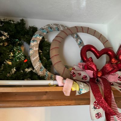 Assorted seasonal wreaths, including a green pine wreath, a burlap spring wreath, and a Valentine's Day wreath with a red glitter...