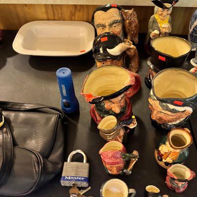 Collection of vintage ceramic character jugs and mugs in various sizes, displayed alongside a Master Lock with keys, a blue Eveready...