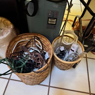 Two woven wicker baskets filled with various electrical cords, power strips, and cables, shown alongside a portable oxygen concentrator...