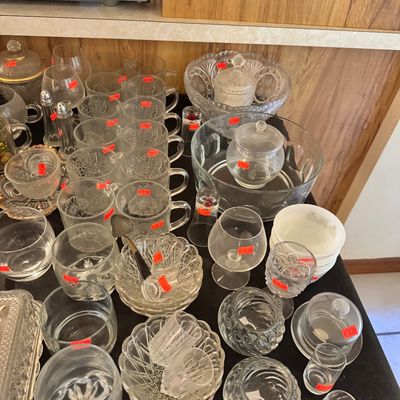 Assortment of vintage glassware, including patterned mugs, serving bowls, lidded jars, and drinking glasses, arranged on a black tabletop.