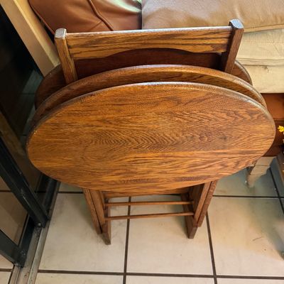 Set of vintage wooden folding TV tray tables with a matching storage stand, featuring an oval design and a warm oak finish.