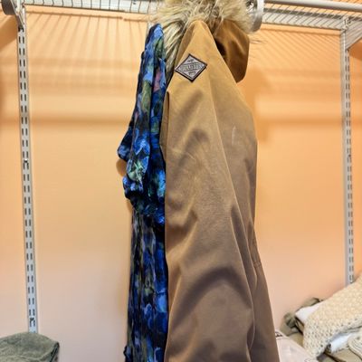 Hollister tan winter parka with a faux-fur trimmed hood, hanging in a closet alongside a blue patterned garment.