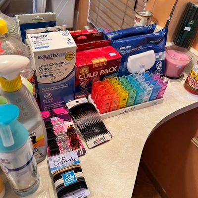 Assorted personal care and household items, including a multi-colored monthly pill organizer, hair accessories, lens cleaning wipes, and...