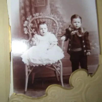 Antique sepia-toned studio portrait of two young children, housed in an embossed cardboard mat, circa late 19th or early 20th century.