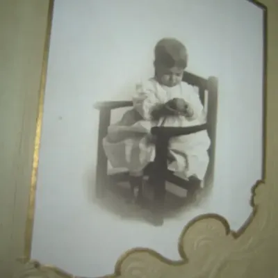 Antique black and white cabinet card portrait of a baby in a high chair, housed in an ornate embossed paper frame.