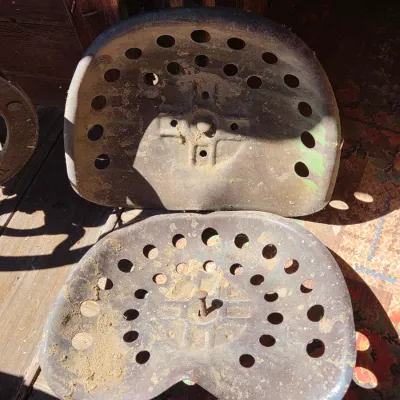 Two vintage steel tractor seats - one partially green