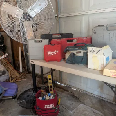 Sale Photo Thumbnail #99: Assorted power tools and equipment, including a large Lasko industrial pedestal fan, a Milwaukee tool case, a Bucket Master tool organizer, and a Makita angle grinder in its original box.