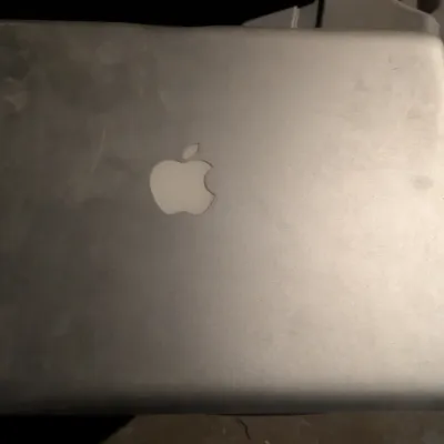 Sale Photo Thumbnail #102: Older model Apple MacBook laptop with a silver aluminum finish, showing some surface wear and smudging on the outer lid.