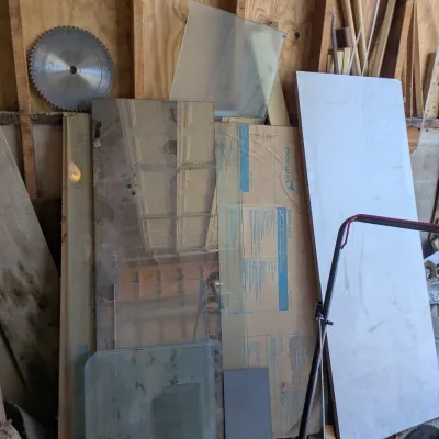 Sale Photo Thumbnail #116: Assorted sheets of glass, Plexiglas, and plywood leaning against a workshop wall, accompanied by a circular saw blade.