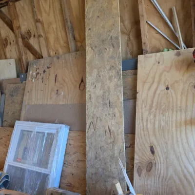 Sale Photo Thumbnail #117: Assorted construction materials including plywood sheets, oriented strand board (OSB), and a new-in-wrap vinyl window, stored in a shed alongside a red string trimmer.