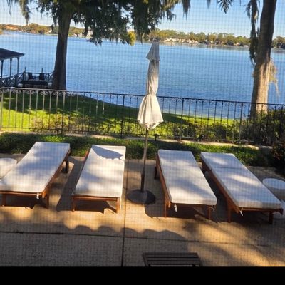 Set of four wooden outdoor chaise lounges with white cushions, accompanied by a matching patio umbrella and two small side tables.