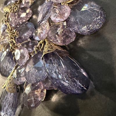 purple crystal type statement necklace featuring faceted teardrop beads suspended from a gold-tone chain.