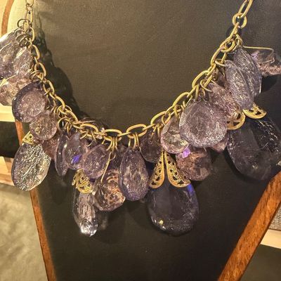 purple crystal type statement necklace featuring faceted teardrop beads suspended from a gold-tone chain.