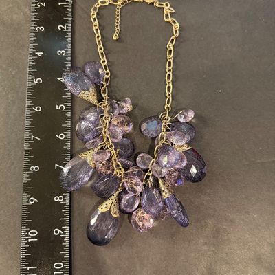 purple crystal type statement necklace featuring faceted teardrop beads suspended from a gold-tone chain.