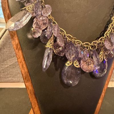 purple crystal type statement necklace featuring faceted teardrop beads suspended from a gold-tone chain.