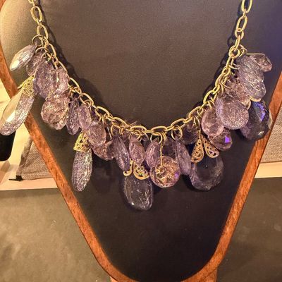 purple crystal type statement necklace featuring faceted teardrop beads suspended from a gold-tone chain.