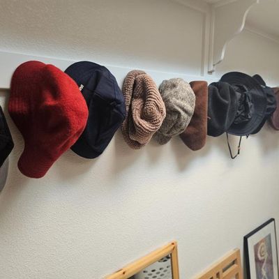 Assortment of men's and women's hats, including baseball caps, newsboy caps, and bucket hats, hanging on a wall-mounted rack.