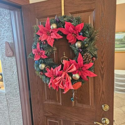 Festive artificial Christmas wreath decorated with red poinsettias, a large red bow, pinecones, and gold and purple ornaments
