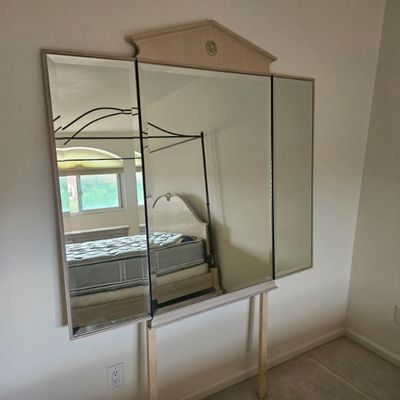 Vintage tri-fold dresser mirror with a pediment top featuring a decorative medallion, mounted on wooden support posts.