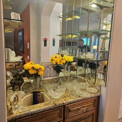 Built-in wet bar featuring a granite countertop, wooden cabinetry, and a mirrored back wall with glass shelving displaying various...