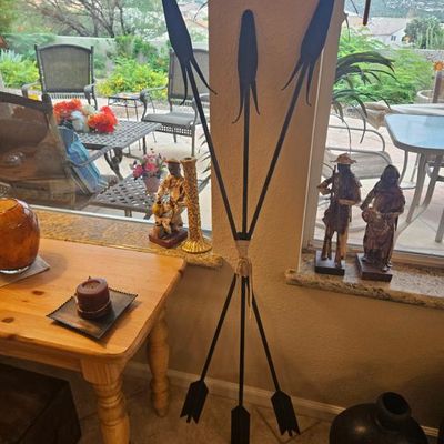 Rustic metal decorative arrow tripod sculpture tied with twine, displayed alongside Southwest-style figurines and pottery.