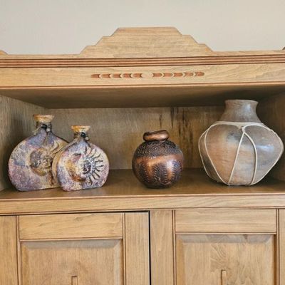 Collection of Southwestern-style decorative pottery, including sun-and-moon motif flasks and a clay pot with cord wrapping, displayed on...