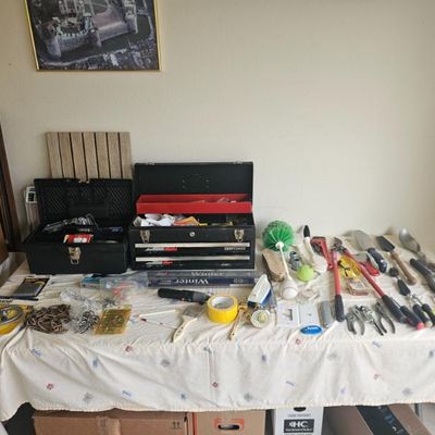 Assortment of hand tools, hardware, and toolboxes, including a black Craftsman metal toolbox, displayed on a table.