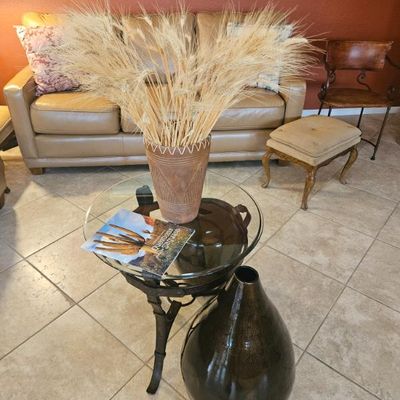 Southwestern-style home decor featuring a glass-top metal side table with a dried wheat arrangement in a textured clay pot, accompanied...