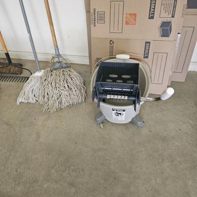 Commercial-style rolling mop bucket with wringer, accompanied by two string mops and a stack of unused Home Depot cardboard moving boxes.