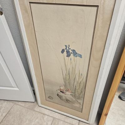 Framed Asian-style watercolor painting depicting blue irises and a bird on a rock, presented in a white frame with a wide fabric mat.