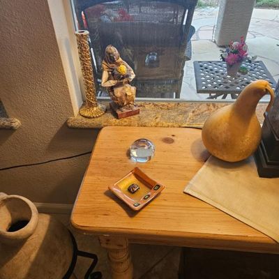 Assorted home decor items including a small glass dish, a dried gourd, and a paper mache figurine displayed on a light wood side table.