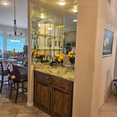 Built-in wet bar featuring a granite countertop, rustic wooden cabinetry, and a mirrored back wall with glass shelving displaying glassware.