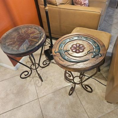 Pair of rustic round side tables featuring carved wooden tops with celestial and floral motifs on scrolled wrought iron bases.