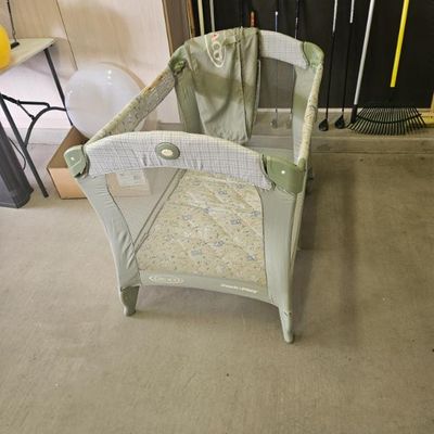 Graco Pack 'n Play portable playard in sage green and plaid, showing light wear from use.
