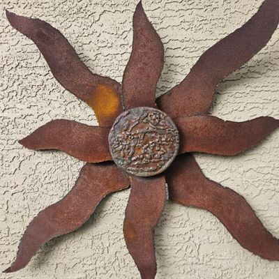 Rustic metal sunburst wall art featuring a heavily rusted finish and a textured, circular center.