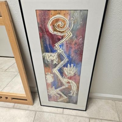 Framed mixed-media artwork featuring Southwestern petroglyph-style motifs, including a Kokopelli figure, a spiral, and a horned animal,...