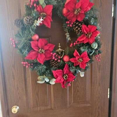 Festive Christmas wreath featuring artificial pine boughs, large red poinsettias, pinecones, and red berry accents,