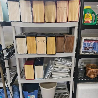 Four-tier grey plastic shelving unit holding various office supplies, including expanding file folders and three-ring binders.