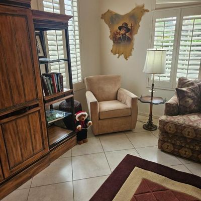 Living room furniture including a tall wooden media cabinet, a beige upholstered armchair, a traditional floor lamp with an integrated...